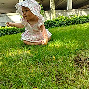 Clairissa is registered to the contest to win money with this photo: baby, child, toddler, sitting, grass, outdoor, garden, bonnet, dress, pink, frills, face, portrait, looking_sideways, sunlight, greenery, tree, building, lawn, exploring
