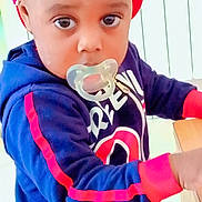 Ychane a rejoint le concours — aidez-le/la à gagner de superbes lots ! toddler, child, pacifier, red_cap, hoodie, navy_blue, red_stripes, yellow_skirt, indoor, looking_at_camera, curious, young_child, person, clothing, hand, wooden_surface, face, headwear, expression, casual