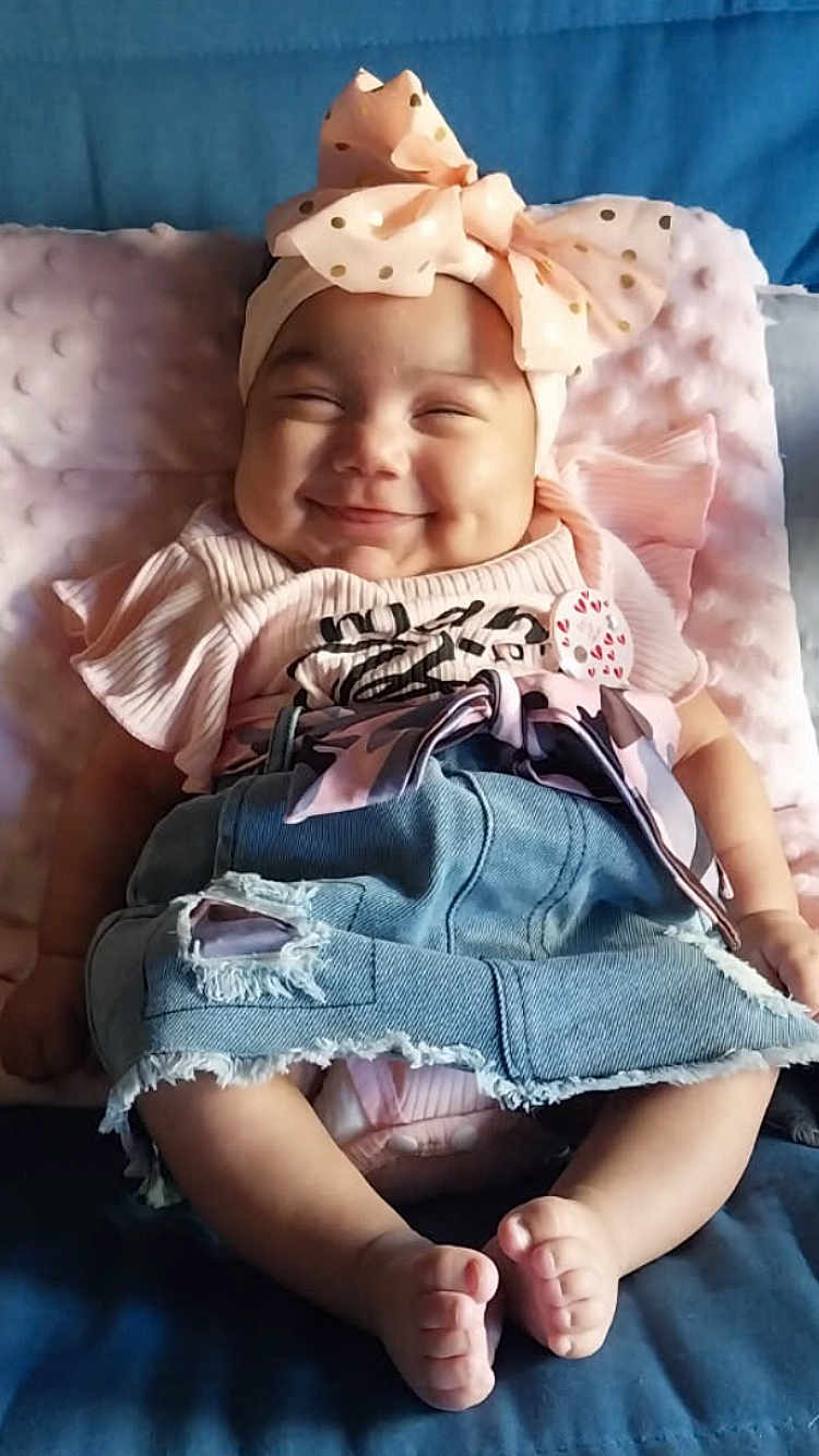 Sakinah participe au concours pour gagner de l'argent avec cette photo : baby, smiling, headband, bow, pink, cushion, denim_skirt, ripped_skirt, barefoot, cute, happy, infant, clothing, fabric, sitting, child, face, portrait, indoors, soft