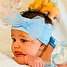 baby, blue_bow, headband, infant, child, portrait, closeup, soft_lighting, doll, blue_eyes, cute, resting, hand, bracelet, silk, fabric, indoor, skin, young_child, face
