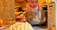 Indira is registered to the contest to win money with this photo: baby, chef_hat, baking, kitchen, mixing_bowl, bread, eggs, milk_carton, wooden_cabinets, countertop, apron, infant, food_preparation, cooking, child, indoor, candid, portrait, cute, domestic