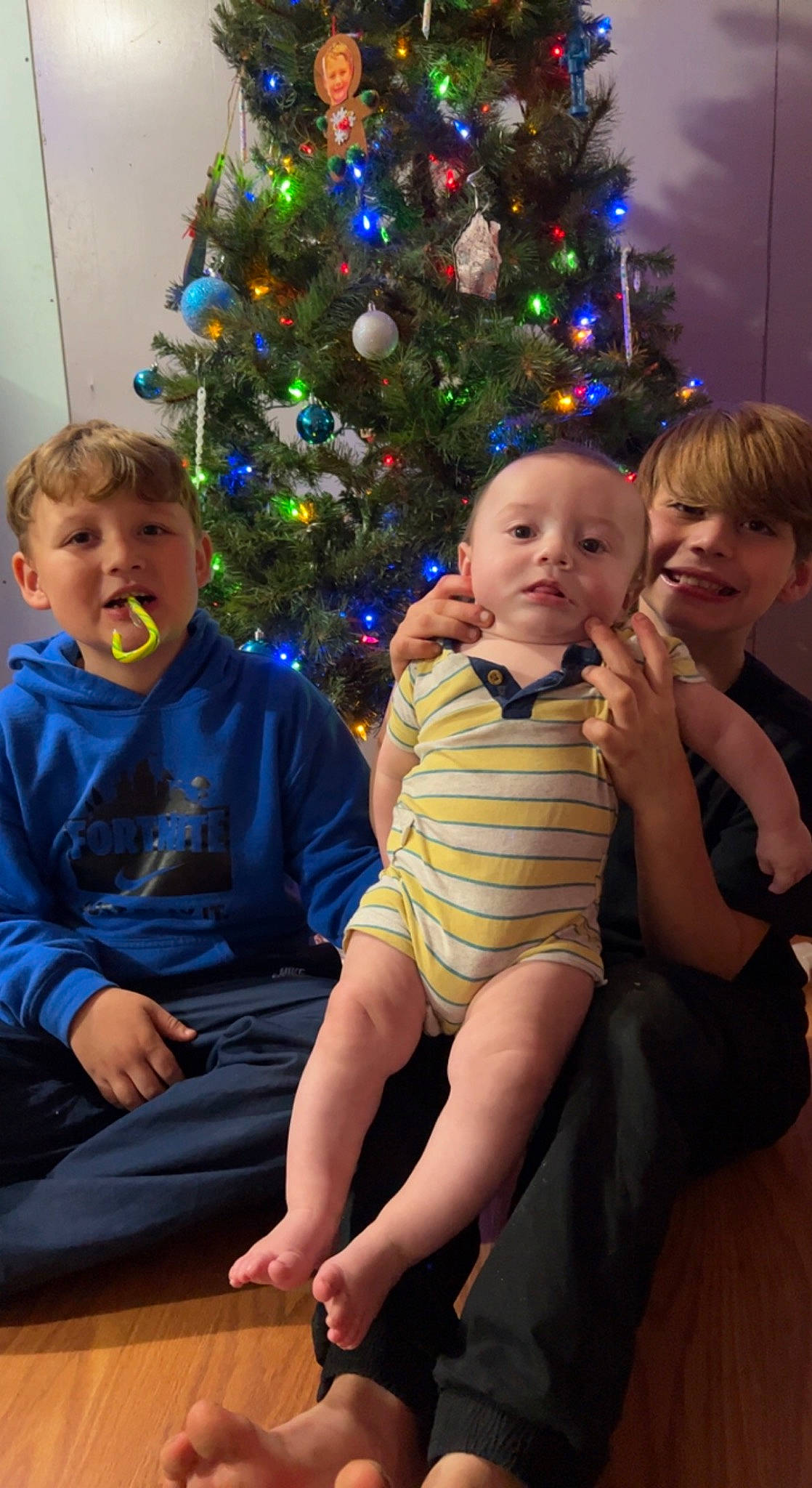 Atlas is registered to the contest to win money with this photo: arm, baby_toddler_clothing, child, christmas, christmas_decoration, christmas_ornament, christmas_tree, event, face, fun, happy, head, holiday_ornament, iris, joy, lap, person, skin, smile, standing