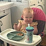toddler, high_chair, snack, sippy_cup, kitchen, smile, child, face, eating, furniture, floor, foot, clothing, person, plastic_plate, baby, indoor, expression, seat, table