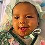 Yona is registered to the contest to win money with this photo: baby, smiling, face, bonnet, clothing, embroidery, green, child, portrait, happy, cute, infant, headwear, closeup, person, indoors, soft_light, fabric, colorful, expression