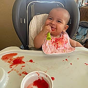 Yona joined the competition — help win amazing prizes! baby, high_chair, bib, messy, food, spoon, smile, child, indoor, table, feeding, happy, infant, cute, red_food, plastic_cup, seat, person, meal, tongue