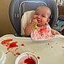 baby, high_chair, bib, messy, food, spoon, smile, child, indoor, table, feeding, happy, infant, cute, red_food, plastic_cup, seat, person, meal, tongue