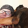 person, dog, glasses, bandana, indoor, closeup, face, ear, brown, black, skin, portrait, cozy, snuggle, pet, companion, casual, headwear, relaxed, human