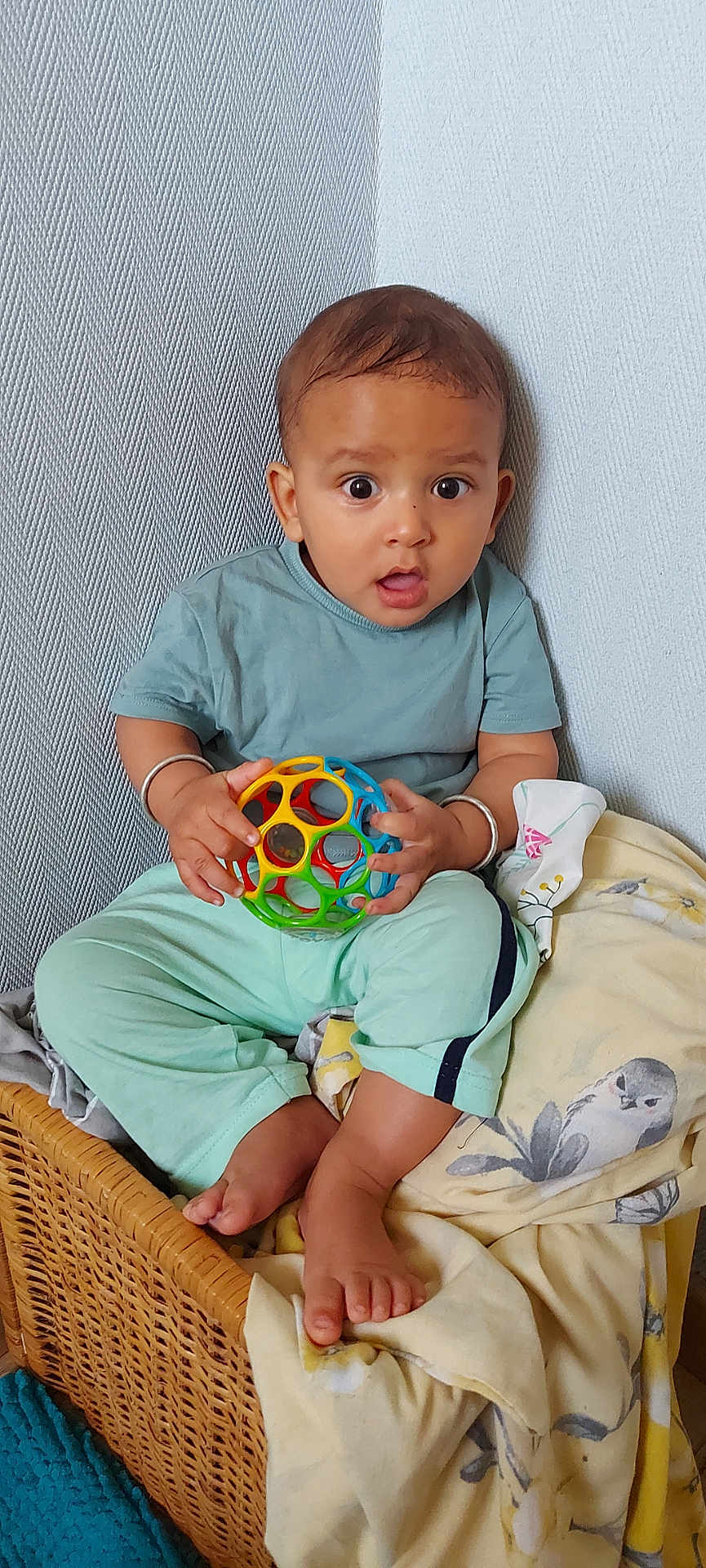 Pragyan a rejoint le concours — aidez-le/la à gagner de superbes lots ! baby, child, toy, ball, wicker_basket, blanket, indoor, curious, wide_eyes, sitting, clothing, foot, hand, person, cute, playful, soft_lighting, expression, casual, home