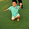 child, boy, grass, outdoor, polo_shirt, shorts, barefoot, green, playing, fun, sunlight, person, kneeling, casual_clothing, daytime, park, happy, movement, adult, background