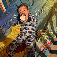 Kaden is registered to the contest to win money with this photo: toddler, child, pajamas, bottle, blanket, bed, face, person, indoor, sleepwear, cute, resting, comfort, colorful, pattern, lying_down, young_child, nursery, cozy, drink