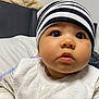 baby, child, face, headwear, striped_hat, bib, indoor, curious, closeup, chubby_cheeks, wide_eyes, infant, clothing, cute, portrait, person, soft_lighting, newborn, young_child, looking_up