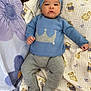 Weston is registered to the contest to win money with this photo: baby, infant, knitwear, blue_hat, blue_sweater, crown_design, blanket, teddy_bear_pattern, purple_flower, cozy, cute, lying_down, clothing, warm, child, person, indoors, soft_toy_pattern, knitted_pants, knitted_booties