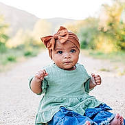 Daphne is registered to the contest to win money with this photo: baby, child, infant, headwrap, bow, green_dress, denim, jeans, barefoot, sitting, outdoor, gravel_path, portrait, bokeh, nature, trees, cute, big_eyes, expression, photography
