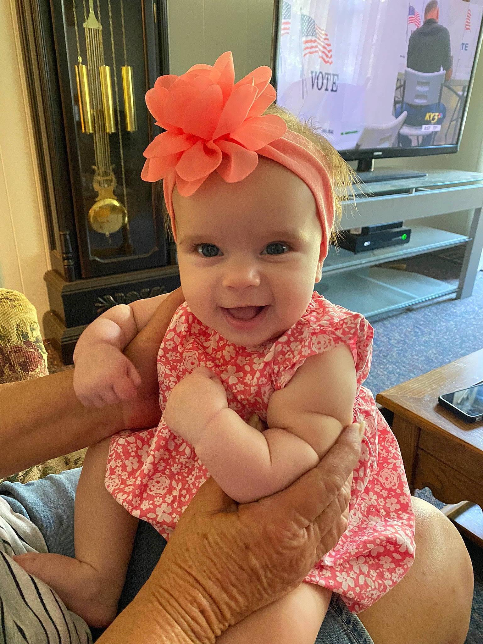 Ember is registered to the contest to win money with this photo: baby, baby_toddler_clothing, blond, chin, curtain, face, finger, happy, hat, headpiece, headwear, human_leg, joy, kitchen_appliance, knee, person, pink, shelf, skin, smile