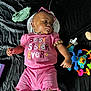 Kahlani is registered to the contest to win money with this photo: accessory, baby, black_background, bracelet, child, colorful, cute, headwear, indoors, infant, lying_down, pacifier, person, pink_clothing, playtime, relaxed, shorts, sunglasses, toy, tshirt