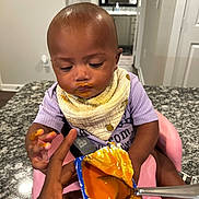 Kahlani joined the competition — help win amazing prizes! baby, baby_food, bib, child, clothing, countertop, curious, cute, feeding, granite, hand, highchair, indoor, infant, kitchen, messy_face, orange_food, person, pink_chair, spoon