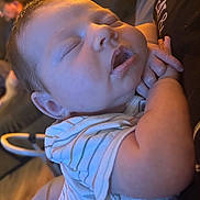 River is registered to the contest to win money with this photo: baby, sleeping, infant, person, face, arm, clothing, striped_shirt, chubby_cheeks, mouth_open, indoor, warm_lighting, hand, closeup, peaceful, newborn, soft_skin, rest, cuddle, portrait