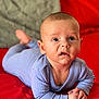 baby, infant, blue_clothing, red_background, lying_down, hands_clasped, curious, wide_eyes, soft_skin, indoor, portrait, child, cute, small_hands, early_morning_light, cozy, comfortable, expression, human, toddler