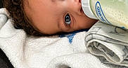 Akai is registered to the contest to win money with this photo: baby, blanket, blue_eyes, bottle, child, close_up, comfort, couch, cozy, curly_hair, face, feeding, indoor, infant, lying_down, milk, person, portrait, resting, soft_texture