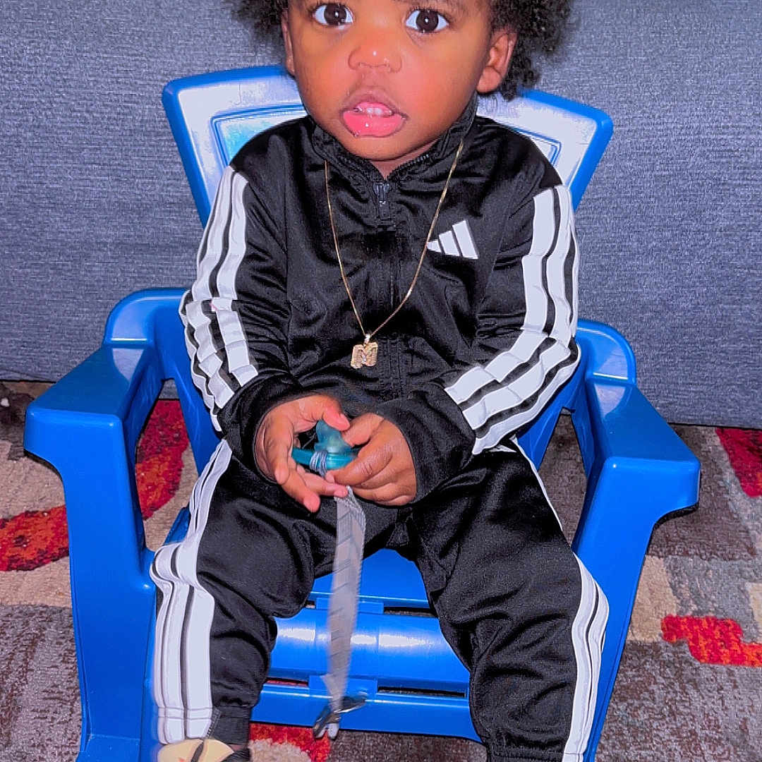 Markiem joined the competition — help win amazing prizes! black_tracksuit, blue_chair, carpet, child, clothing, curly_hair, expression, floor, footwear, indoor, necklace, pacifier, person, portrait, sitting, sneakers, toddler, toy, white_stripes, young_child