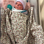 Addilyn joined the competition — help win amazing prizes! newborn, baby, infant, child, face, portrait, hospital, bassinet, blanket, swaddled, floral, pacifier, hat, cap, pink, white, lying_down, indoors, medical_setting, sleeping_area