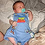 baby, newborn, pacifier, toy_story, clothing, blue_romper, blanket, infant, cute, sleepwear, foot, hand, lying_down, indoor, person, child, soft_texture, expression, resting, cozy