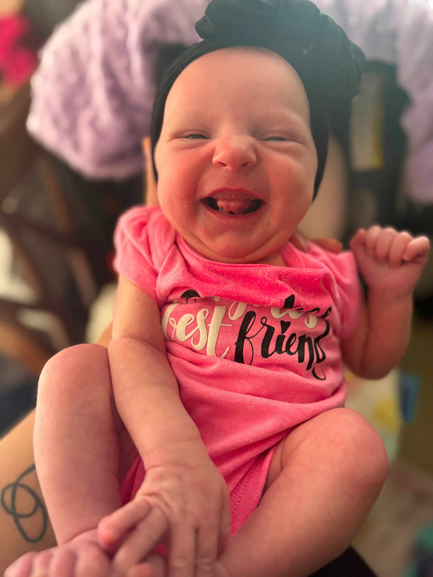 Ella is registered to the contest to win money with this photo: baby, infant, smile, headband, pink_clothing, onesie, face, hands, legs, tattoo, person, happy, closeup, portrait, child, cute, expression, skin, blurred_background, indoor