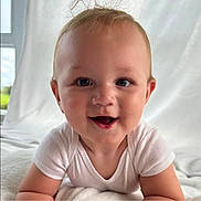 Koda is registered to the contest to win money with this photo: baby, infant, smiling, face, white_clothing, blanket, indoor, cute, happy, child, skin, head, eyes, mouth, tongue, arm, light, window, portrait, closeup