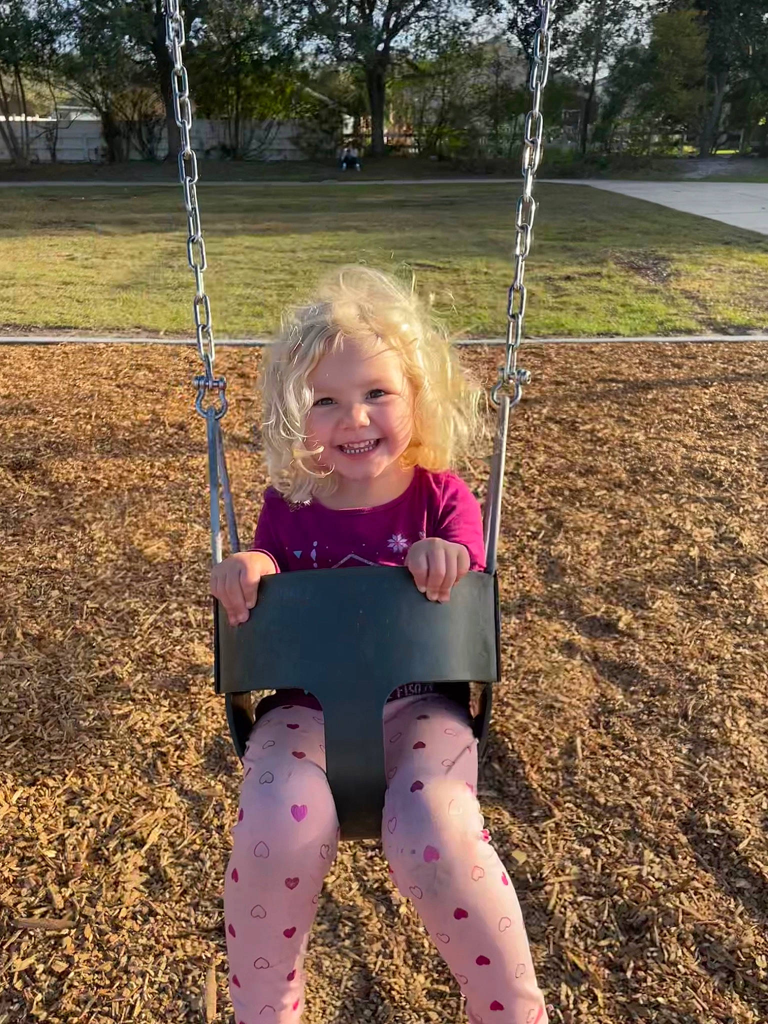 Audrey is registered to the contest to win money with this photo: arm, beauty, fun, grass, happy, human_body, joy, leisure, mammal, nature, people_in_nature, person, plant, playground, public_space, sleeve, smile, summer, swing, toddler