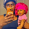Zara joined the competition — help win amazing prizes! adult, baby, mirror_selfie, phone, orange_phone, pink_bonnet, blue_bonnet, tank_top, smiling, holding, indoor, portrait, face, person, digital_overlay, time_display, date_display, hand, skin, clothing