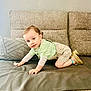 baby, beige_shorts, blue_eyes, child, couch, crawling, curious, face, furniture, green_shirt, hands, indoor, light, pillow, portrait, smiling, sneakers, textured_fabric, toddler, wall