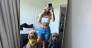 Luna is registered to the contest to win money with this photo: woman, mirror, selfie, kitten, dog, bandana, shirt, bedroom, bed, pillow, curtain, ceiling_fan, floor, tile_floor, shorts, crop_top, pet, indoor, reflection, phone