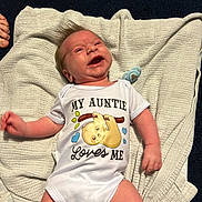 Riley joined the competition — help win amazing prizes! baby, infant, smiling, onesie, blanket, pacifier, cute, happy, clothing, lying_down, indoor, child, newborn, face, hair, human, skin, expression, toddler, love