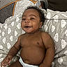 baby, blanket, brown_skin, child, cloud_pattern, curly_hair, cushion, diaper, furniture, happy, home, indoor, infant, lying_down, nursery, photography, pillow, portrait, relaxed, smiling