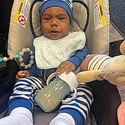 Baby Jojo is registered to the contest to win money with this photo: baby, infant, child, car_seat, carriage, striped_clothing, hat, bib, bottle, plush_toy, stuffed_animal, pacifier_clip, socks, seated, portrait, indoors, vehicle, travel, alert, cute
