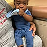 baby, child, infant, sitting, lap, caregiver, portrait, indoor, blue_outfit, bib, hand, chewing, curious, serious_expression, black_socks, furniture, bench, warm_lighting, candid, family
