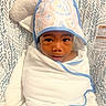 baby, infant, child, portrait, smiling, awake, bonnet, swaddle, blanket, bassinet, crib, nursery, patterned_bedding, animal_print, indoors, lying_down, close_up, face, dark_skin, cozy