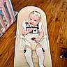 Ember is registered to the contest to win money with this photo: baby, infant, child, bouncer, smiling, headband, socks, white, black_and_white, wooden_floor, indoor, playpen, pet_paw, cute, comfortable, seated, clothing, happy, person, portrait