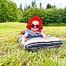 baby, child, sunglasses, red_hat, striped_pillow, grass, outdoor, field, summer, greenery, trees, nature, cute, sun_protection, infant, casual, daylight, fashion, portrait, relaxing