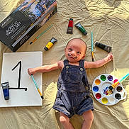 Xyleek is registered to the contest to win money with this photo: baby, infant, paint, acrylic_paint, paint_brush, palette, canvas, number_one, mustache, face_paint, denim_overalls, art_supplies, lying_down, indoors, wrinkled_sheet, colorful, creative, cute, small, expression