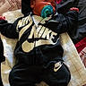 Samaj is registered to the contest to win money with this photo: baby, infant, sleeping, pacifier, nike, hoodie, pants, socks, blanket, bed, patterned_bedding, child, cute, resting, indoors, clothing, relaxation, comfort, young_child, peaceful