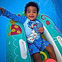 toddler, child, pool, water, inflatable, float, toy, cup, blue, smiling, happy, summer, outdoor, swimwear, shorts, shirt, curly_hair, playful, relaxing, daytime