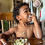 Tamãn is registered to the contest to win money with this photo: casual, child, cream, curly_hair, eating, face, food, hand, happy, indoor, mealtime, messy, natural_light, person, plate, skin, toddler, wooden_chair, wooden_table, young_child