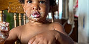 Tamãn is registered to the contest to win money with this photo: brown_skin, child, close_up, curious, curly_hair, dining, eating, expression, face, food, hand, indoor, kid, meal, messy, plate, sitting, table, toddler, wooden_chair