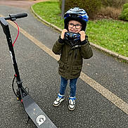 Tyler participe au concours pour gagner de l'argent avec cette photo : child, helmet, electric_scooter, jacket, jeans, sneakers, glasses, smile, outdoor, pavement, path, greenery, bushes, grass, helmet_adjusting, young, happy, urban, recreation, transportation
