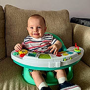 Victor is registered to the contest to win money with this photo: baby, infant, child, toy, striped_shirt, green_seat, couch, beige, smiling, happy, blue_eyes, short_hair, white_socks, navy_shoes, indoor, play, hands, cute, seat, living_room