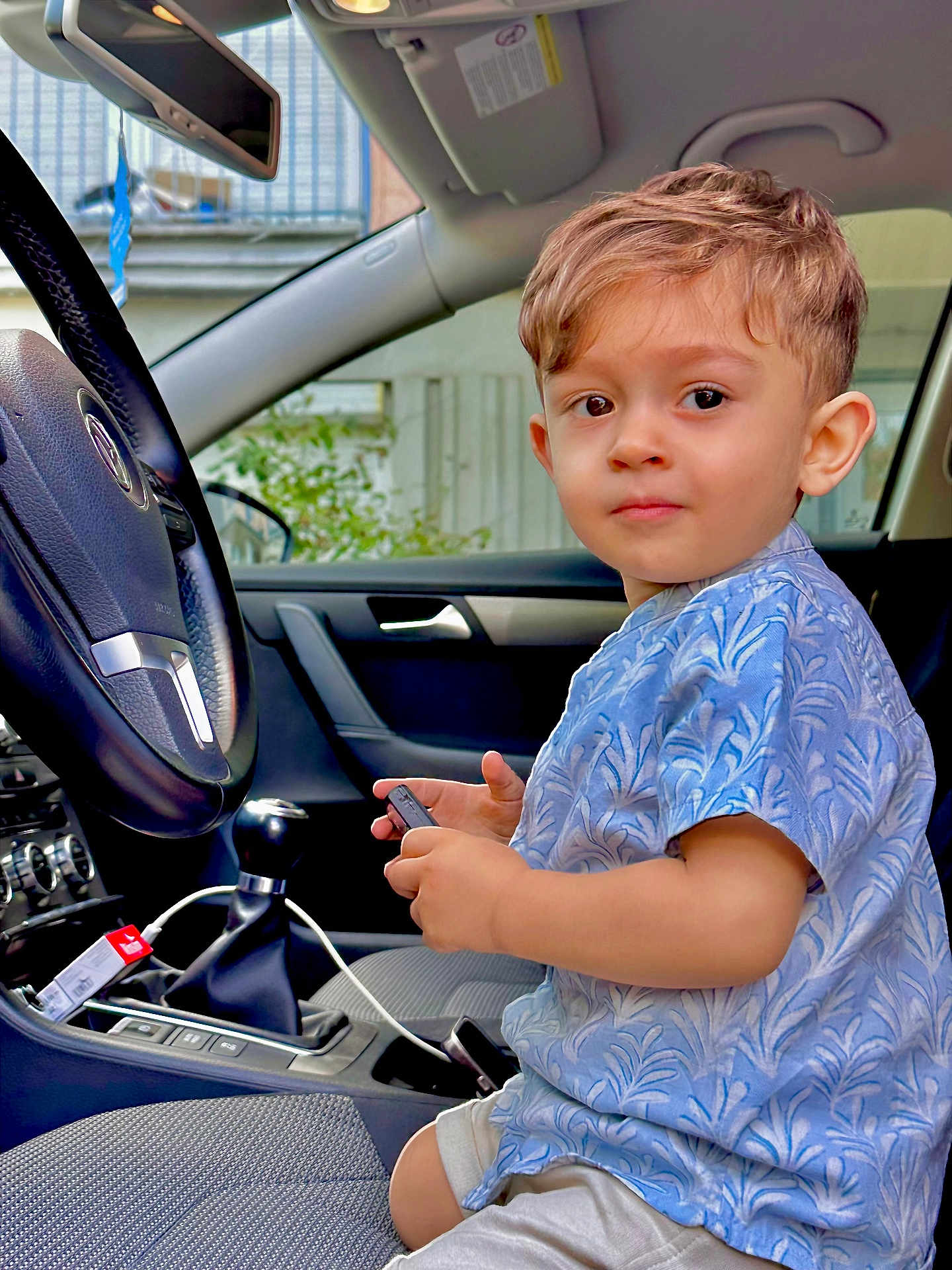 Ahadov Davud a rejoint le concours — aidez-le/la à gagner de superbes lots ! child, toddler, car_interior, steering_wheel, seat, clothing, shorts, blue_shirt, device, window, door, gear_shift, seatbelt, curious, young_boy, indoor, automobile, hands, face, expression