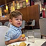 child, boy, food, plate, rice, tomato, fried_food, high_chair, restaurant, indoor, table, glass, drink, clothing, furniture, lighting, expression, sitting, meal, casual