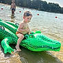 child, toddler, inflatable, crocodile, water, lake, beach, summer, outdoor, sunlight, nature, trees, play, fun, swimwear, sand, reflection, person, water_toy, recreation