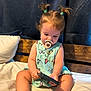 baby, bed, butterfly_pattern, casual, child, curtain, cute, dress, focused, hair_ties, indoor, infant, pacifier, pillow, ponytails, remote_control, sitting, toddler, wooden_headboard, young_child